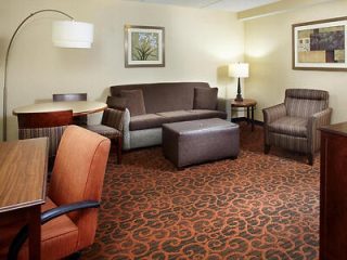 A hotel suite living area with a brown sofa, armchairs, and a work desk on a patterned carpet.